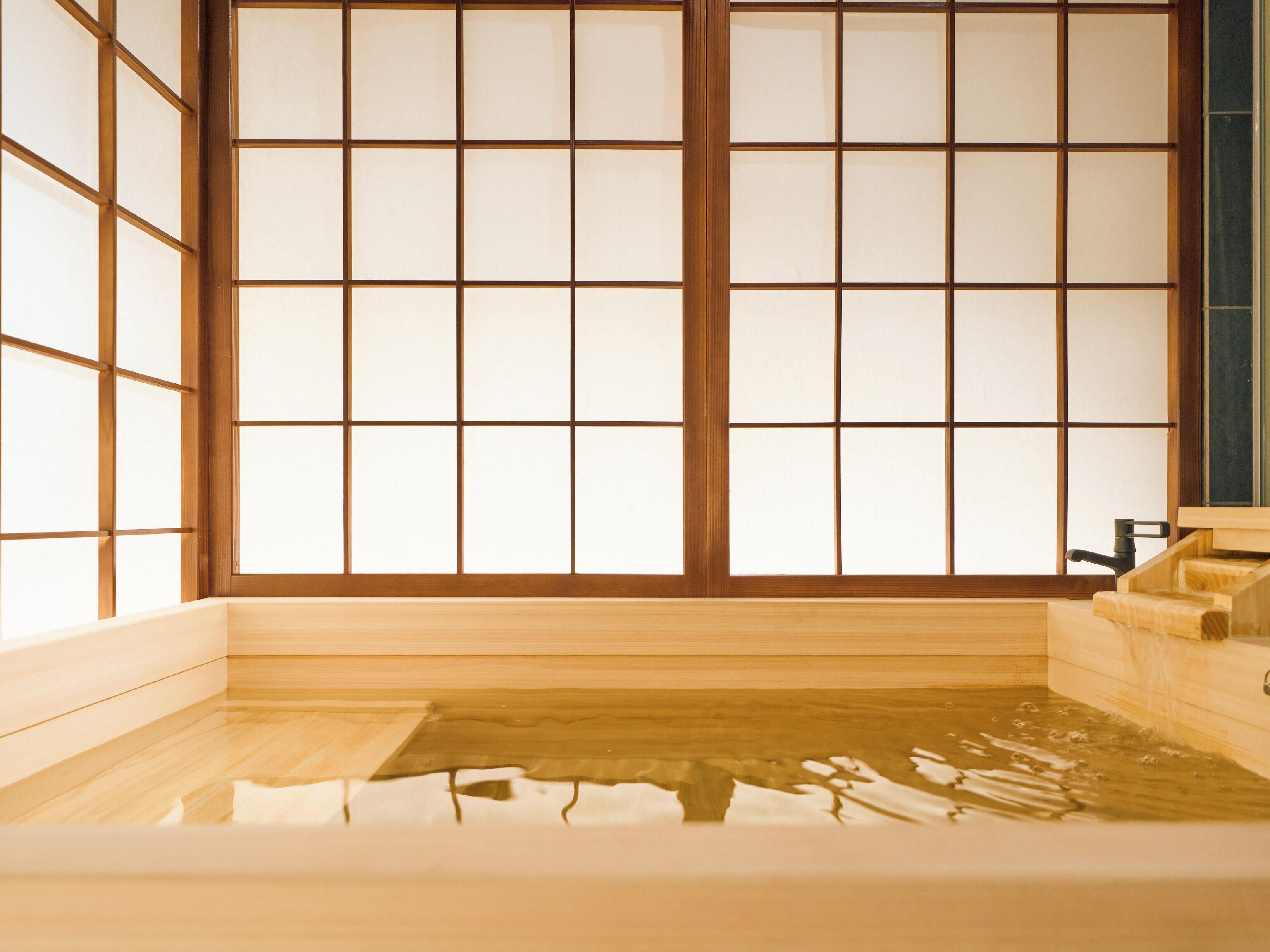 A traditional Japanese onsen with a wooden bath, tiled walls, and a wooden bench.
