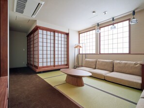 Ein traditioneller japanischer Raum mit Tatami-Boden, einem niedrigen Tisch, einer Couch, verschiebbaren Shoji-Türen und einer hängenden Leuchte.