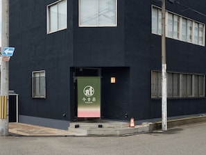 A modern building with a dark facade, a green banner with white text, and a blue directional sign.