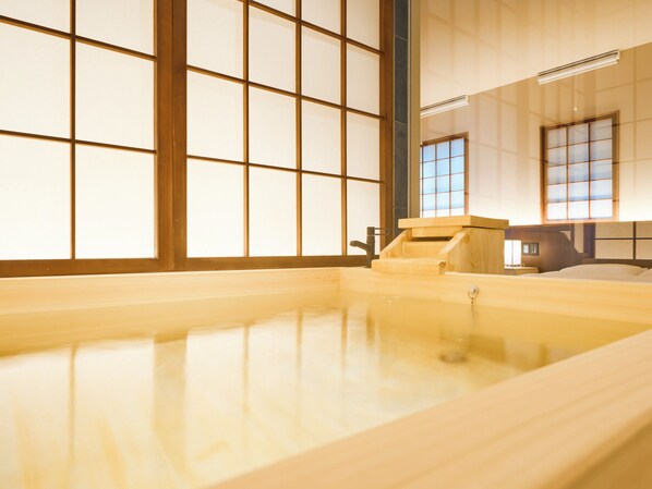 A traditional Japanese onsen with a wooden bath, tiled walls, and a view of the outside through large windows.
