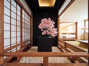 A traditional Japanese-style room with tatami flooring, a black central pillar, and a cherry blossom arrangement.