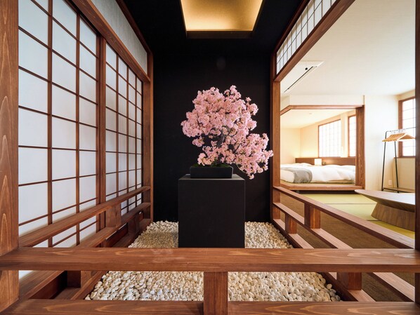 A traditional Japanese-style room with tatami flooring, a black central pillar, and a cherry blossom arrangement.