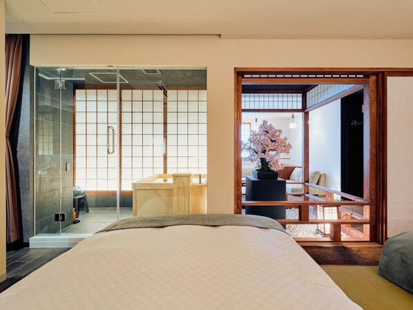 Une chambre moderne avec un grand lit, un bureau en bois et une vue sur une pièce de style japonais traditionnel, visible à travers une porte vitrée.