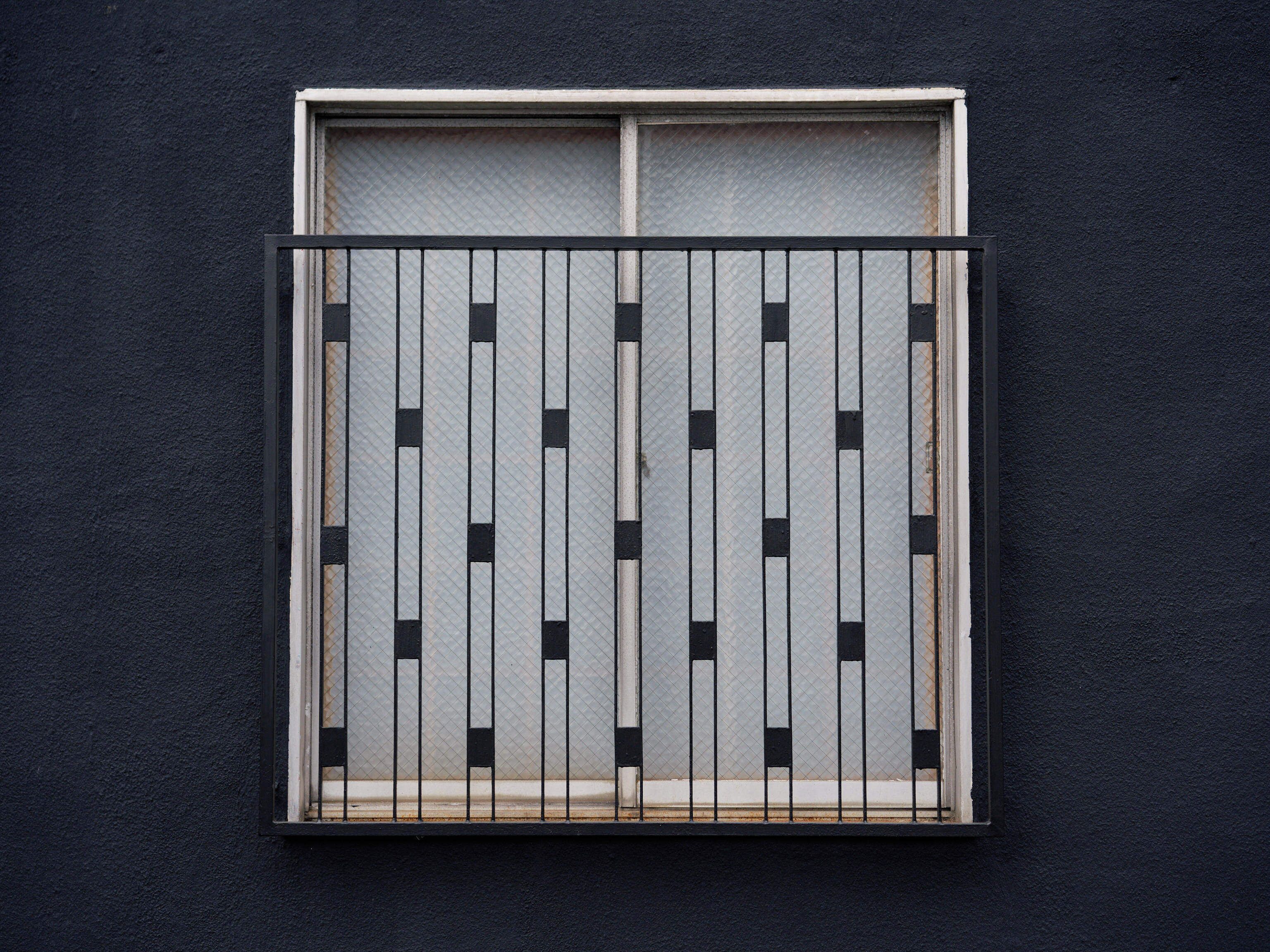 Une fenêtre ornée d’une grille métallique et un mur de couleur sombre.