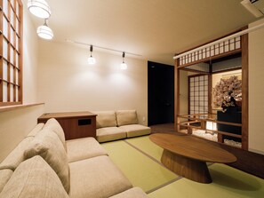 A modern living room with a sectional sofa, a coffee table, and a traditional Japanese sliding door with a flower arrangement.
