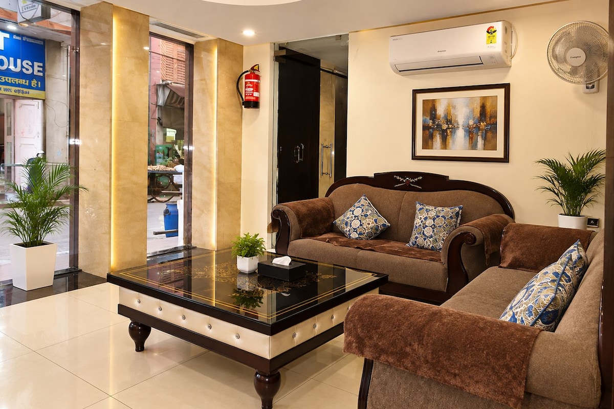 Een hotellobby met een zithoek, een bijzettafeltje, een brandblusser, een airconditioning en een ingelijst schilderij aan de muur.