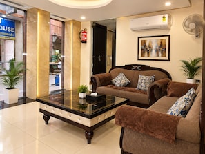 Een hotellobby met een zithoek, een bijzettafeltje, een brandblusser, een airconditioning en een ingelijst schilderij aan de muur.