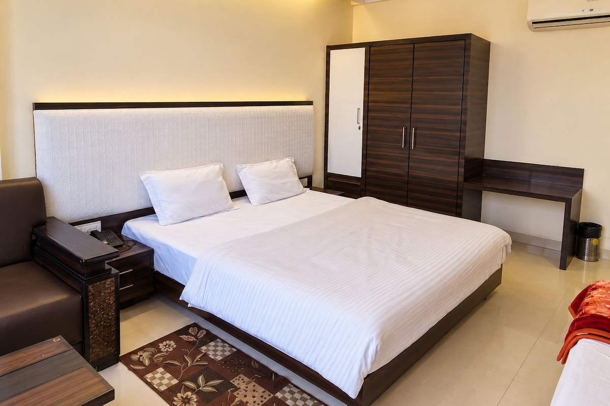 A hotel room with a large bed, a bedside table, a wardrobe, and a desk.