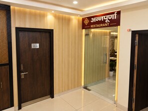 Entrada d'hotel amb un senyal de rentat de mans, una paret de fusta i una porta de vidre que dona a un restaurant.