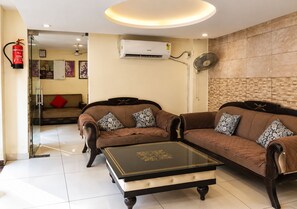 A living room with two sofas, a coffee table, and a wall-mounted air conditioner. - Anand Niketan (Haridwar)