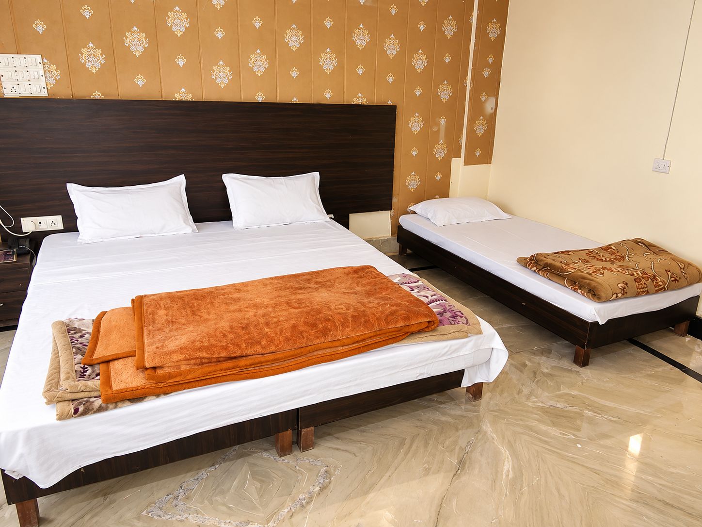 Una habitación de hotel con una cama grande, una cama más pequeña y una mesita de noche con lámpara.