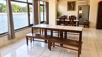A dining area with a view of a body of water, featuring a table and benches, a ceiling fan, and a painting on the wall.