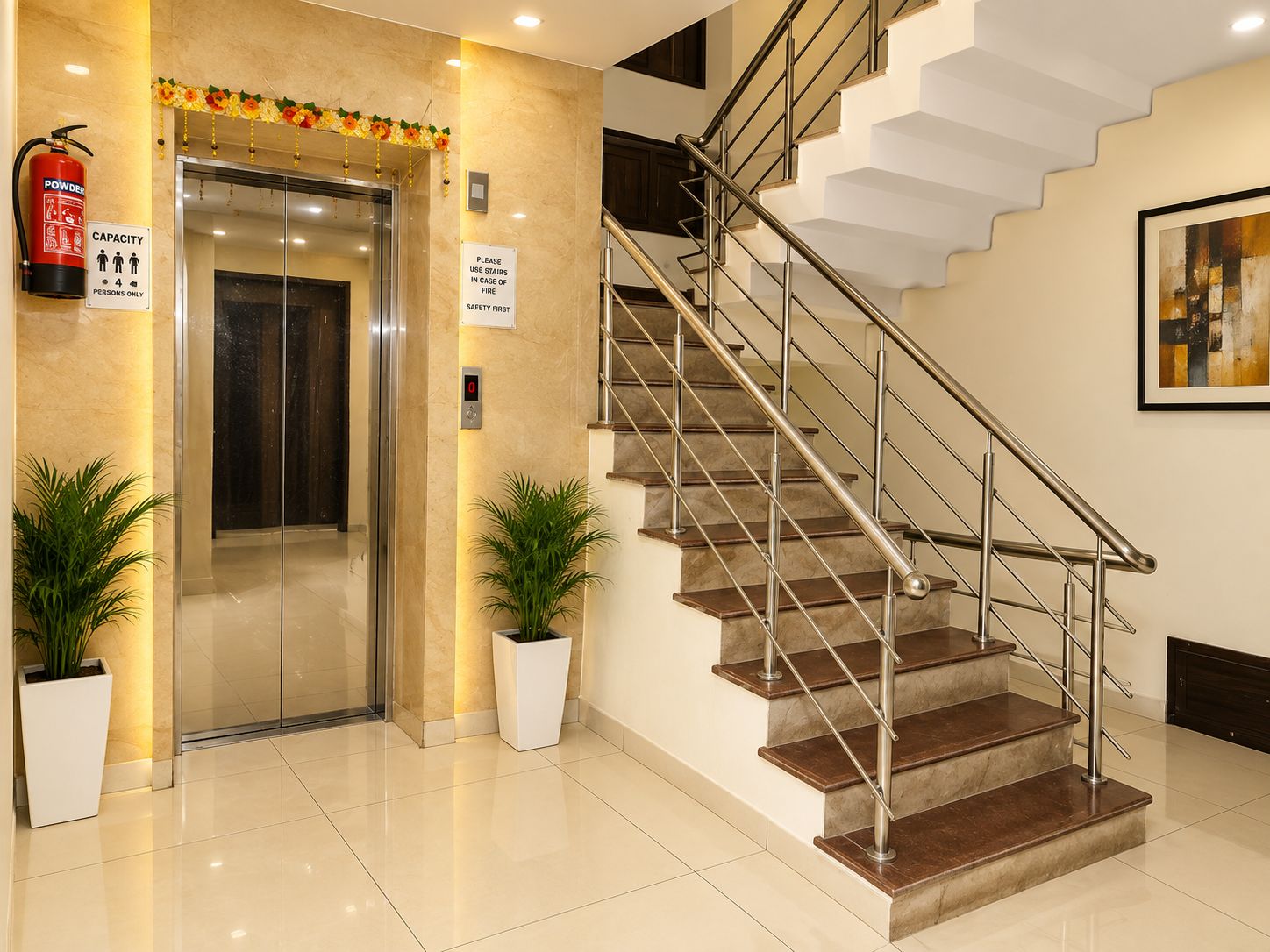 Un vestíbulo de hotel moderno con piso de mármol, una escalera con barandas de metal y un extintor de incendios en la pared.
