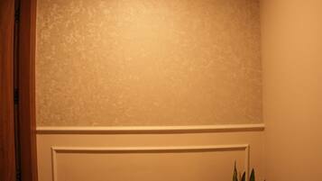 A room with a textured wall, a recessed ceiling light, a white baseboard, and a potted plant.