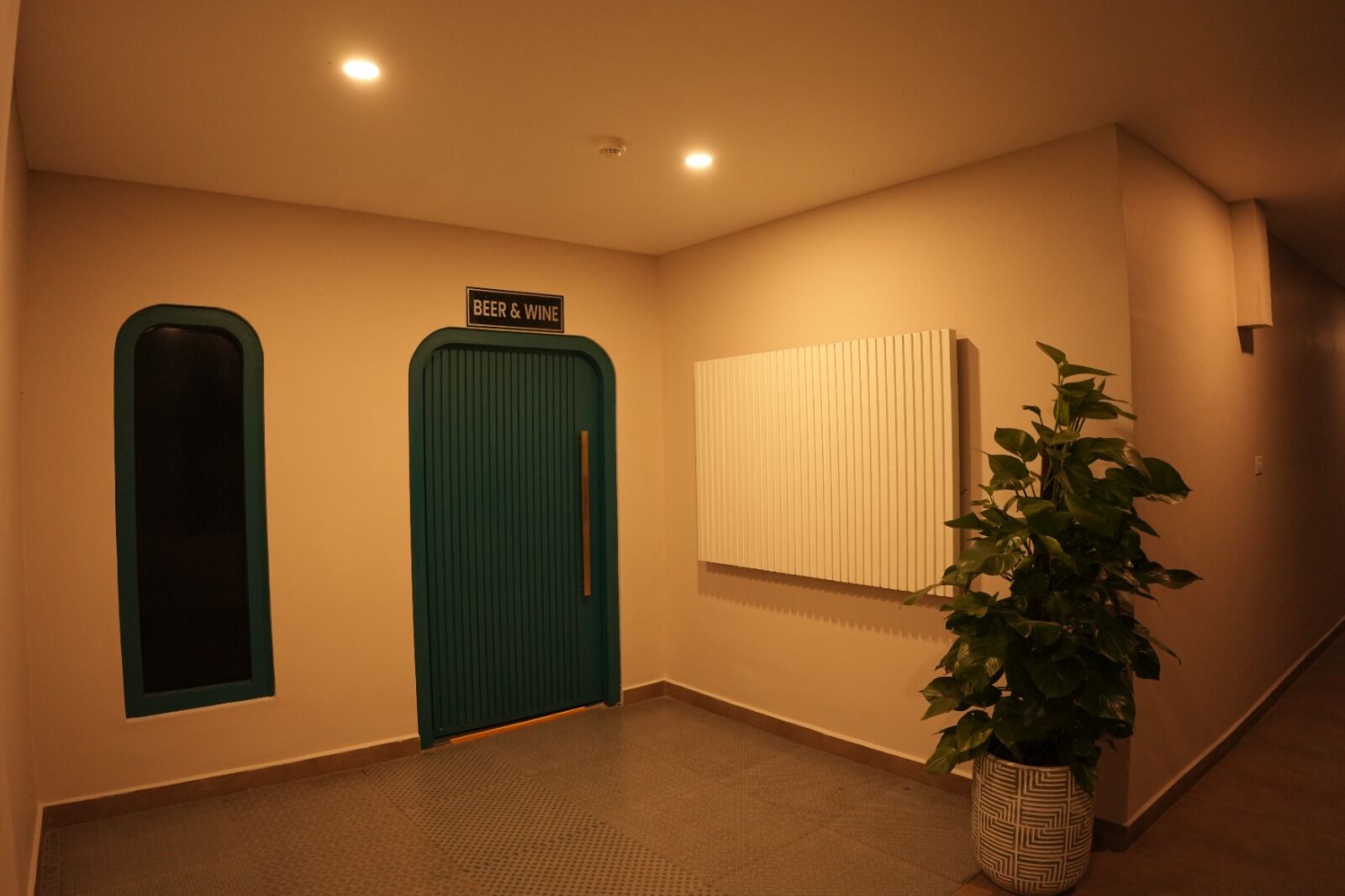 A hallway with two doors labeled 'BEER & WINE,' a potted plant, and a wall-mounted light fixture.