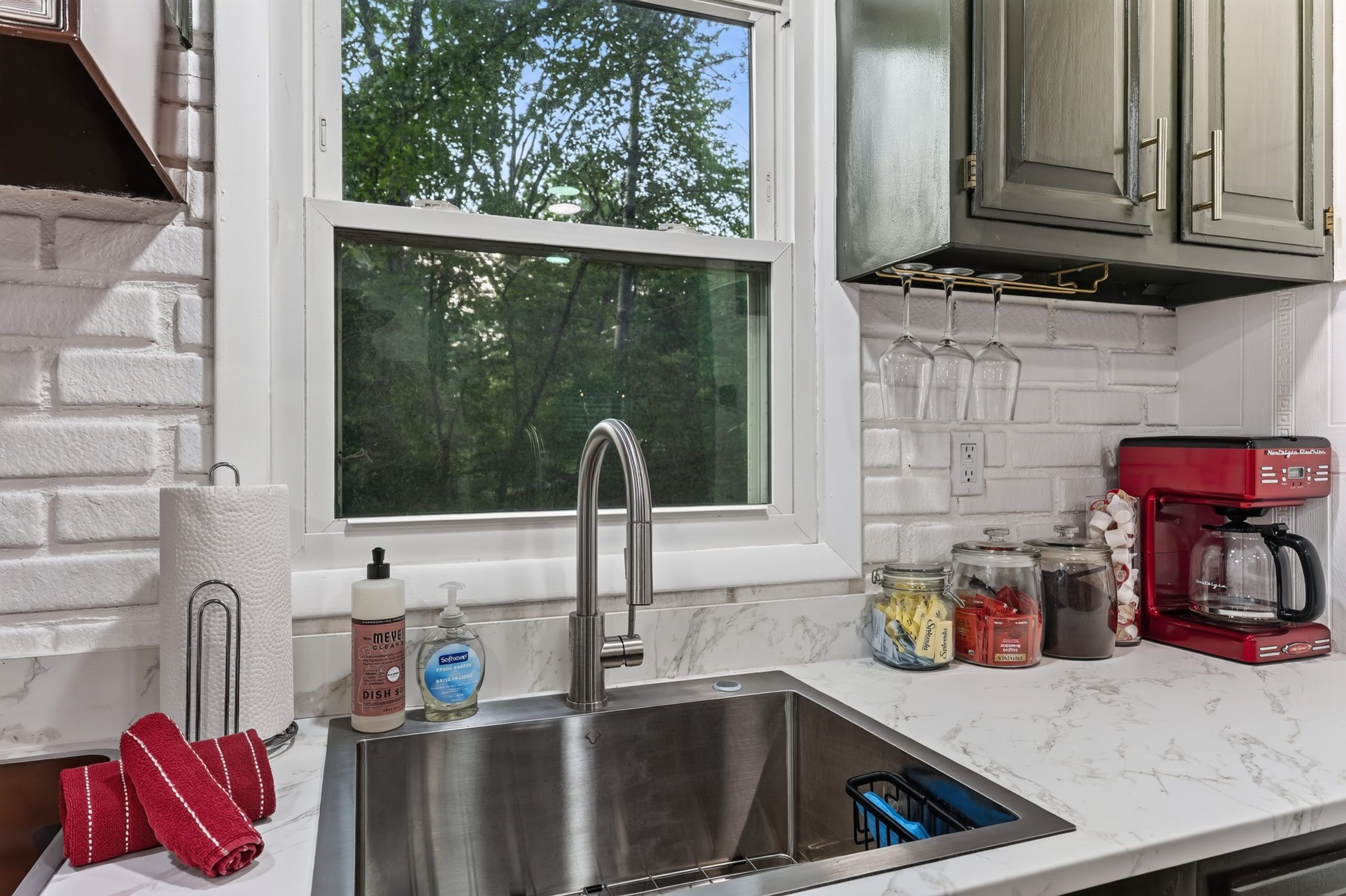 A kitchen with a stainless steel sink, a window, and various kitchen items.