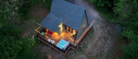 Eine Hütte mit Terrasse, Whirlpool und Sitzbereich im Freien, umgeben von Bäumen.