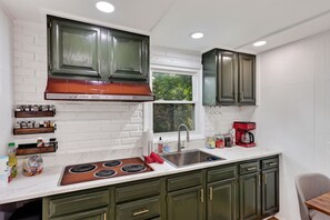 Una cocina con gabinetes verdes, un lavamanos de acero inoxidable y una cafetera roja.