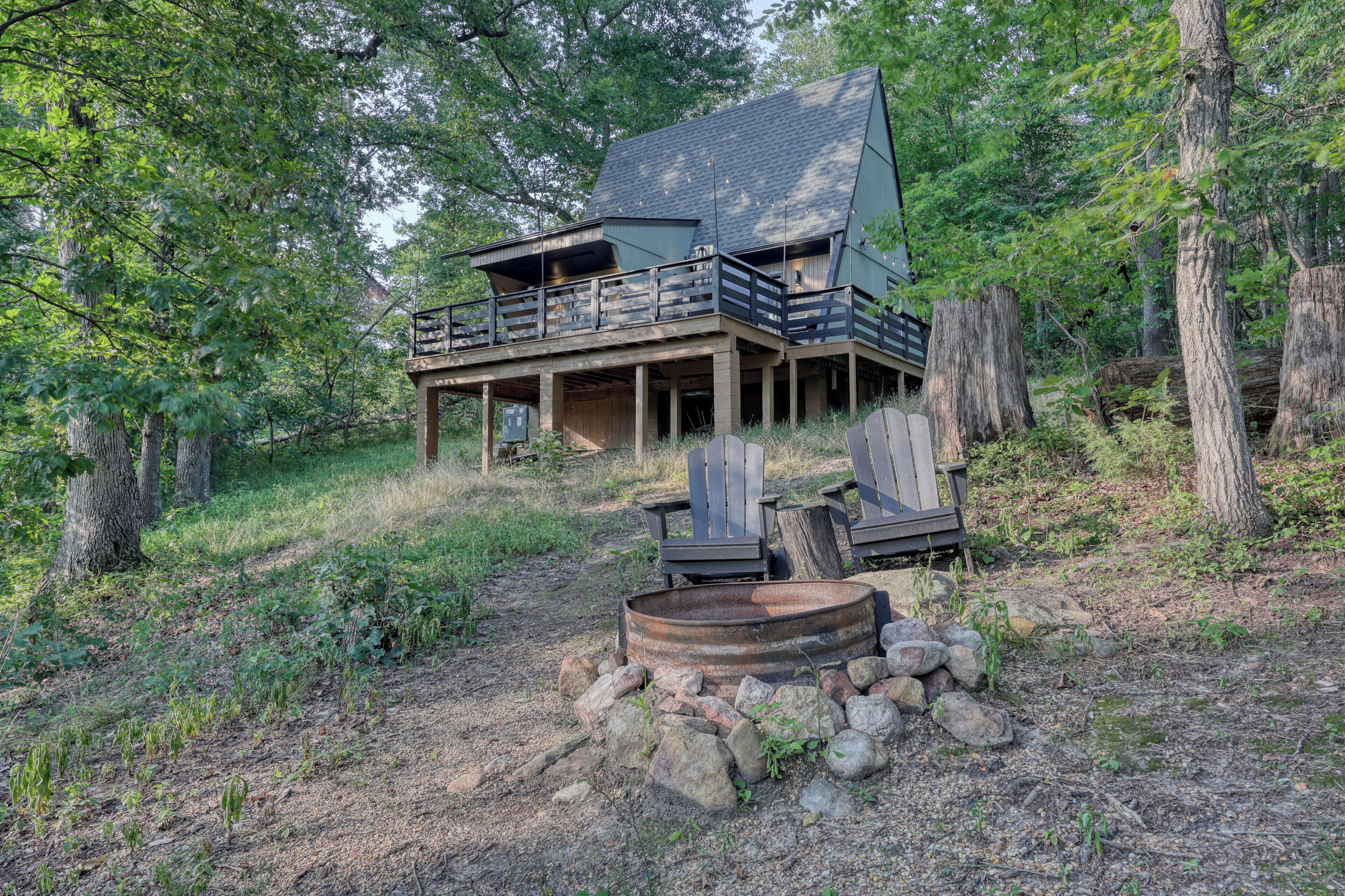 A cabin with a balcony, surrounded by trees and a fire pit.