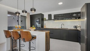 A modern kitchen with a central island, bar stools, pendant lighting, and built-in appliances. - Villa Baculla by Villas Guide (Makarska)
