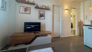Ett vardagsrum med en tv på ett träställ, en dörr som leder till ett badrum och en väggmonterad lampa.