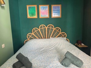 Ein Bett mit Kopfteil im Blattmuster, einer gemusterten Bettdecke und drei gerahmten Bildern an der Wand.
