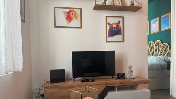 Ett modernt vardagsrum med en tv, ett skrivbord i trä, en liten Buddha-staty och en säng med en unik sänggavel.