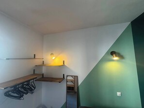 Ein Zimmer mit geneigter Decke, Holzregalen, einem Metallgestell und zwei Wandleuchten.