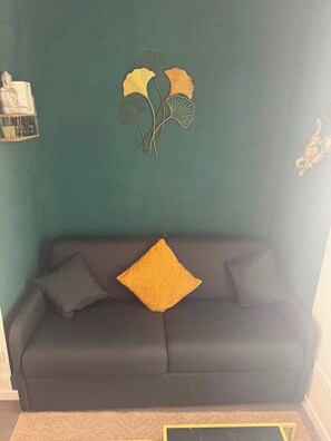 Ein dunkelgraues Sofa mit einem gelben und einem schwarzen Kissen vor einer türkisfarbenen Wand.