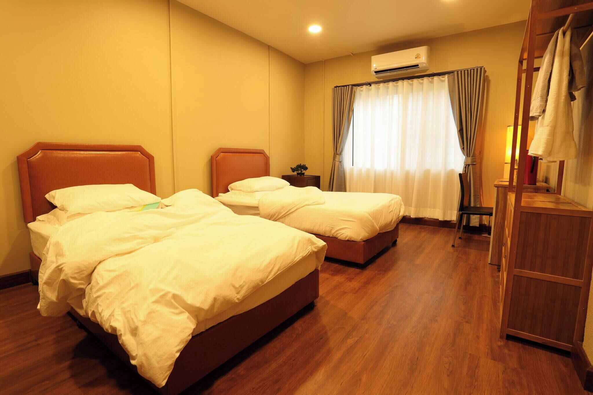 Habitación de hotel con dos camas, aire acondicionado, armario de madera y ventana con cortinas.