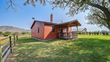 A small, single-story wooden house with a fenced yard and a clear view of the surrounding landscape.