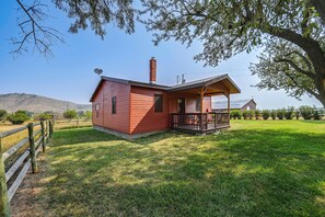 Una pequeña casa de madera de un piso, con patio cercado y vista despejada del paisaje circundante.