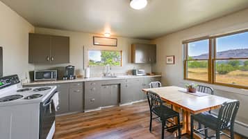 A kitchen with a stove, microwave, and sink, a dining table with chairs, and a window with a view of the outdoors.