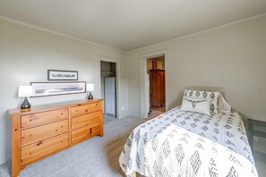 Un dormitorio con un aparador de madera, una cama con ropa de cama estampada, un cuadro enmarcado sobre el aparador y una puerta que da a otra habitación.