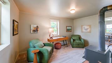 A cozy living room with a fireplace, green armchairs, a wooden coffee table, and artwork on the walls.
