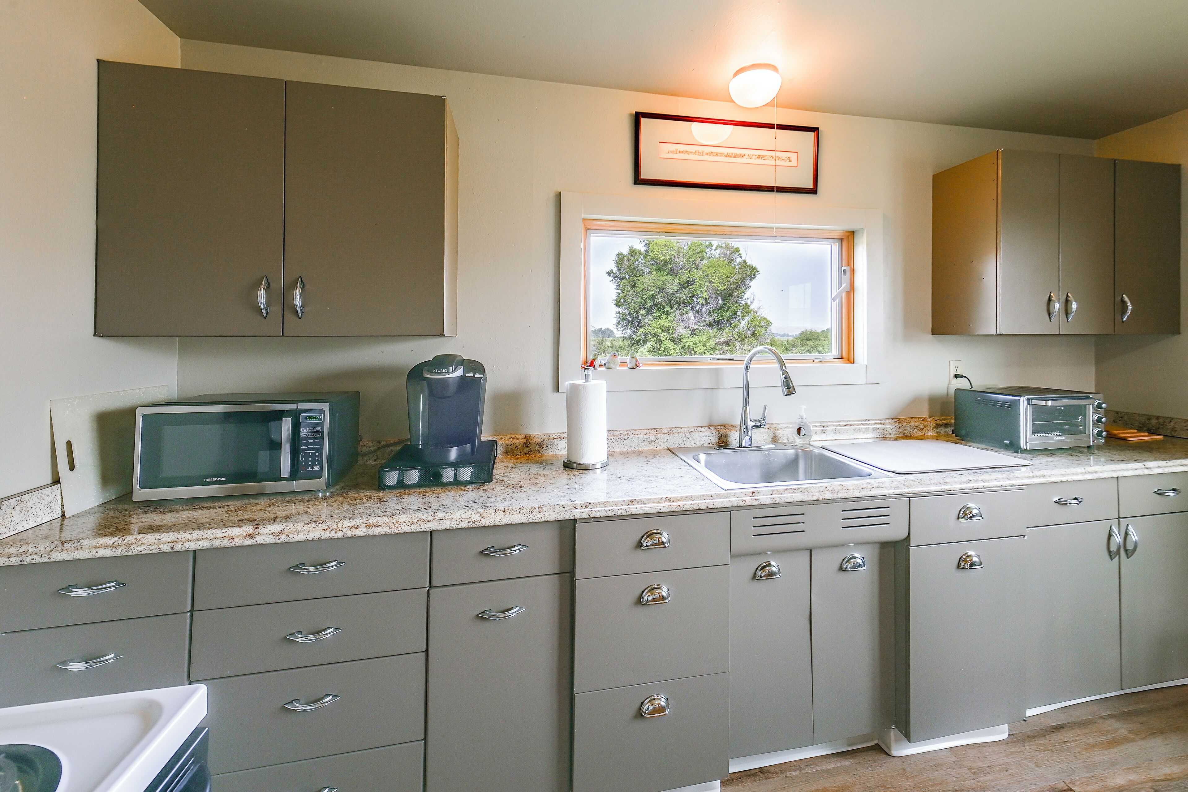 A kitchen with a window, a sink, a microwave, a toaster, and cabinets.