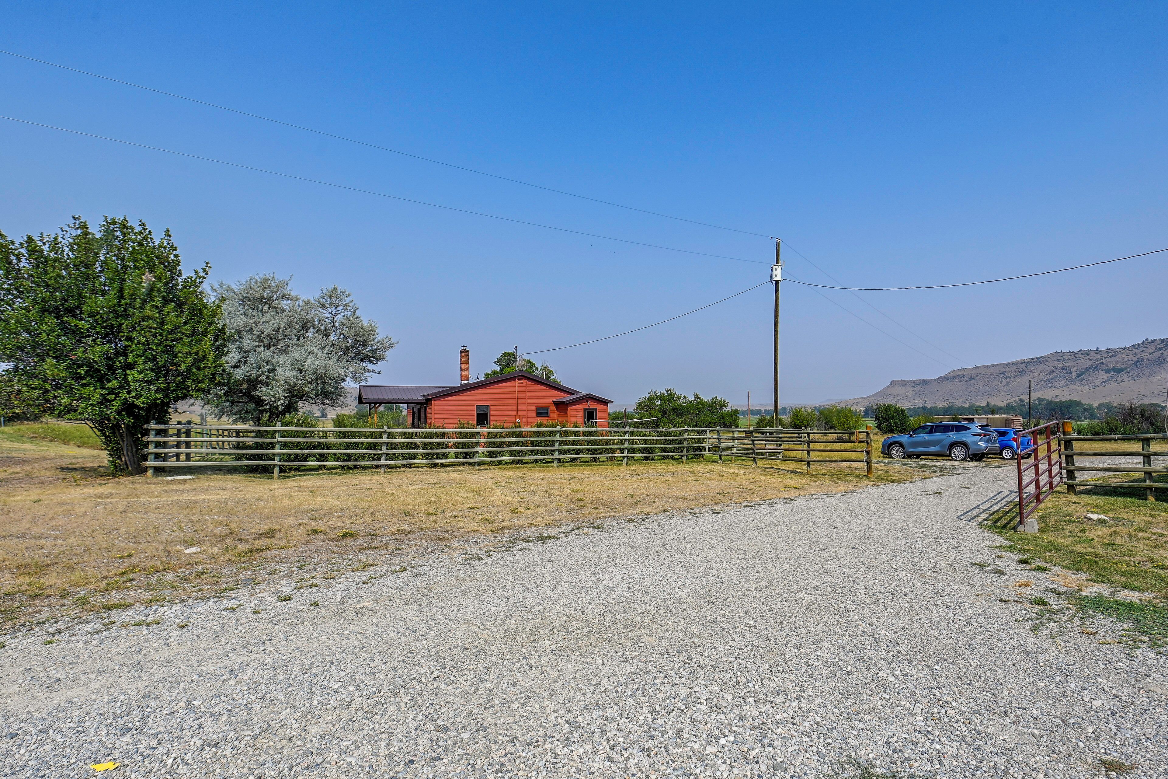 A gravel driveway leading to a red barn with a wooden fence and a blue car parked nearby.