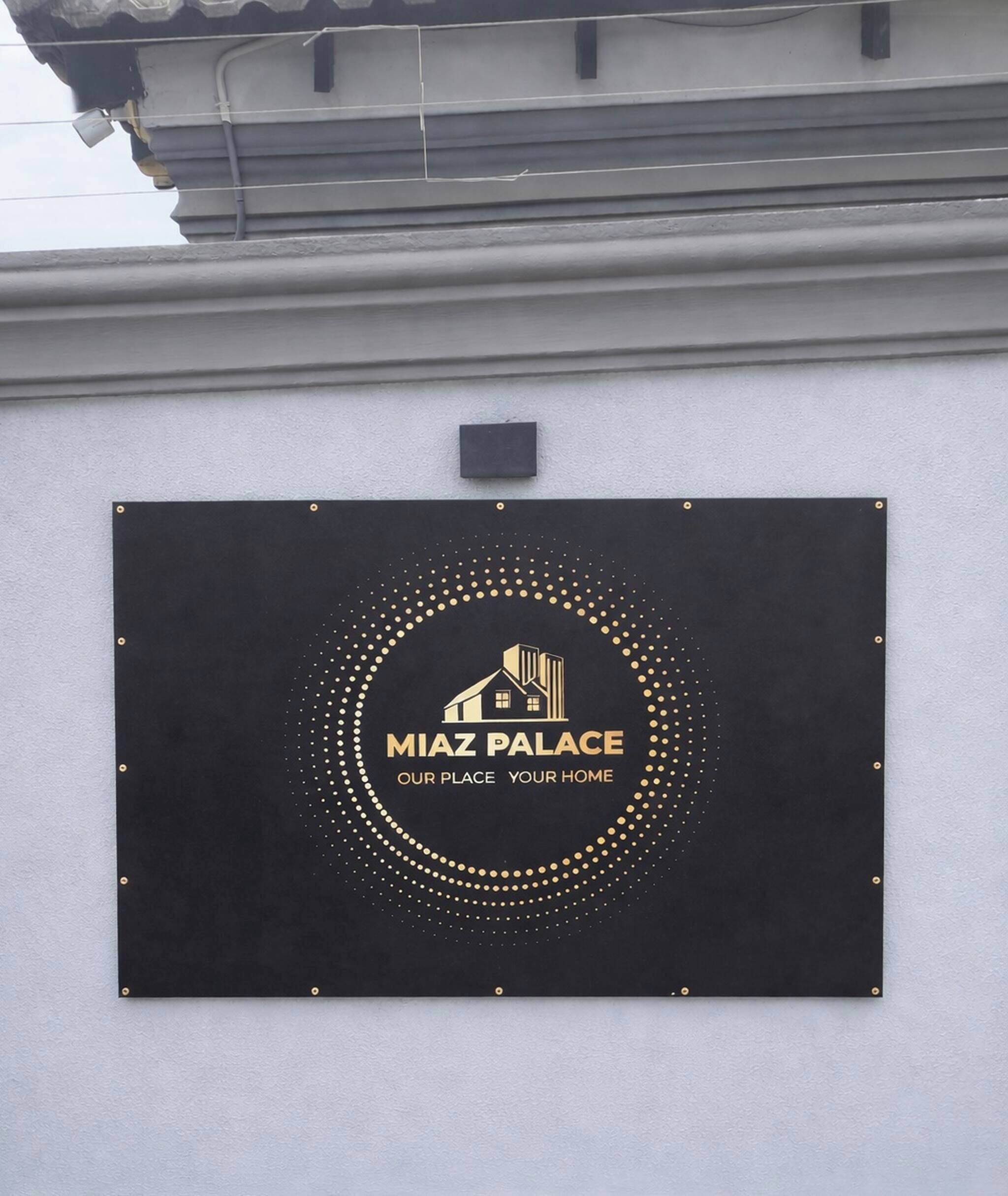 A black sign with gold lettering and a building icon, mounted on a white wall.