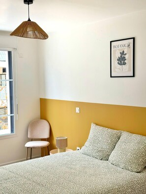 A bedroom with a bed, a chair, a bedside table, a lamp, and a framed botanical print on the wall. - Charming Colombes Apartment  Comfort, Convenience, and Style (Colombes)