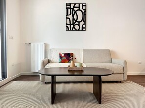 A living room with a sofa, a coffee table, and a decorative wall piece. - Charming Colombes Apartment  Comfort, Convenience, and Style (Colombes)