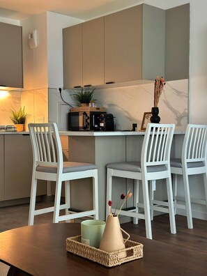 A modern kitchen with white cabinetry, a coffee machine, and two white chairs. - Charming Colombes Apartment  Comfort, Convenience, and Style (Colombes)