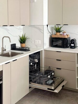 A modern kitchen with a built-in dishwasher, a sink, and a microwave on a white countertop. - Charming Colombes Apartment  Comfort, Convenience, and Style (Colombes)