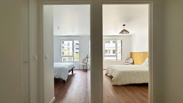 Ein Zimmer mit zwei Betten, einem Sessel und einem Fenster.