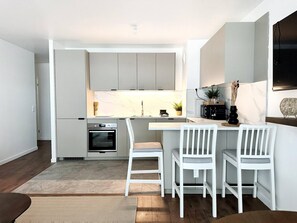 A modern kitchen with a built-in oven, a dining area with white chairs, and a small island with a sink. - Charming Colombes Apartment  Comfort, Convenience, and Style (Colombes)