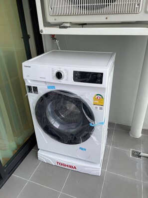A white Toshiba washing machine with a control panel, a digital display, and a protective plastic cover.