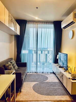 A modern living room with a sofa, a television, and a patterned rug. - Accommodations room with balcony view Sukhumvit77 (Khet Suan Luang)