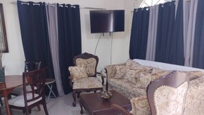 A living room with a sofa, two armchairs, a coffee table, and a flat-screen TV mounted on the wall.