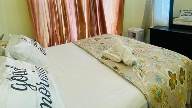 A hotel room with a bed, curtains, a desk with a mirror, and a ceiling fan.