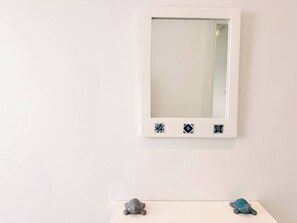 A white wall with a framed mirror and two small turtle figurines on a white surface below. - Appartement Rayhana Sidi Bou Said (Sidi Bou Said)