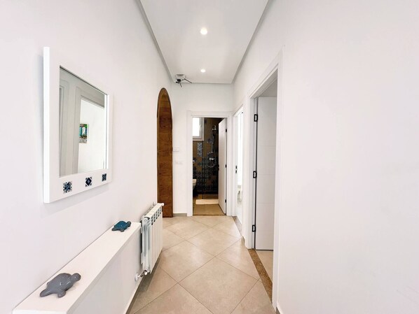 A hallway with a white wall, a large mirror, a radiator, and a door leading to a bathroom. - Appartement Rayhana Sidi Bou Said (Sidi Bou Said)